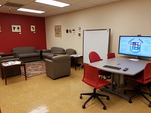 Couches, movable whiteboard, and rolling chairs around a large screen in Animal Health Library.