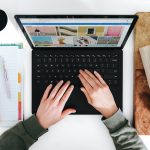 View from above a laptop with hands preparing to type surrounded by a planner with pens and a cup of coffee